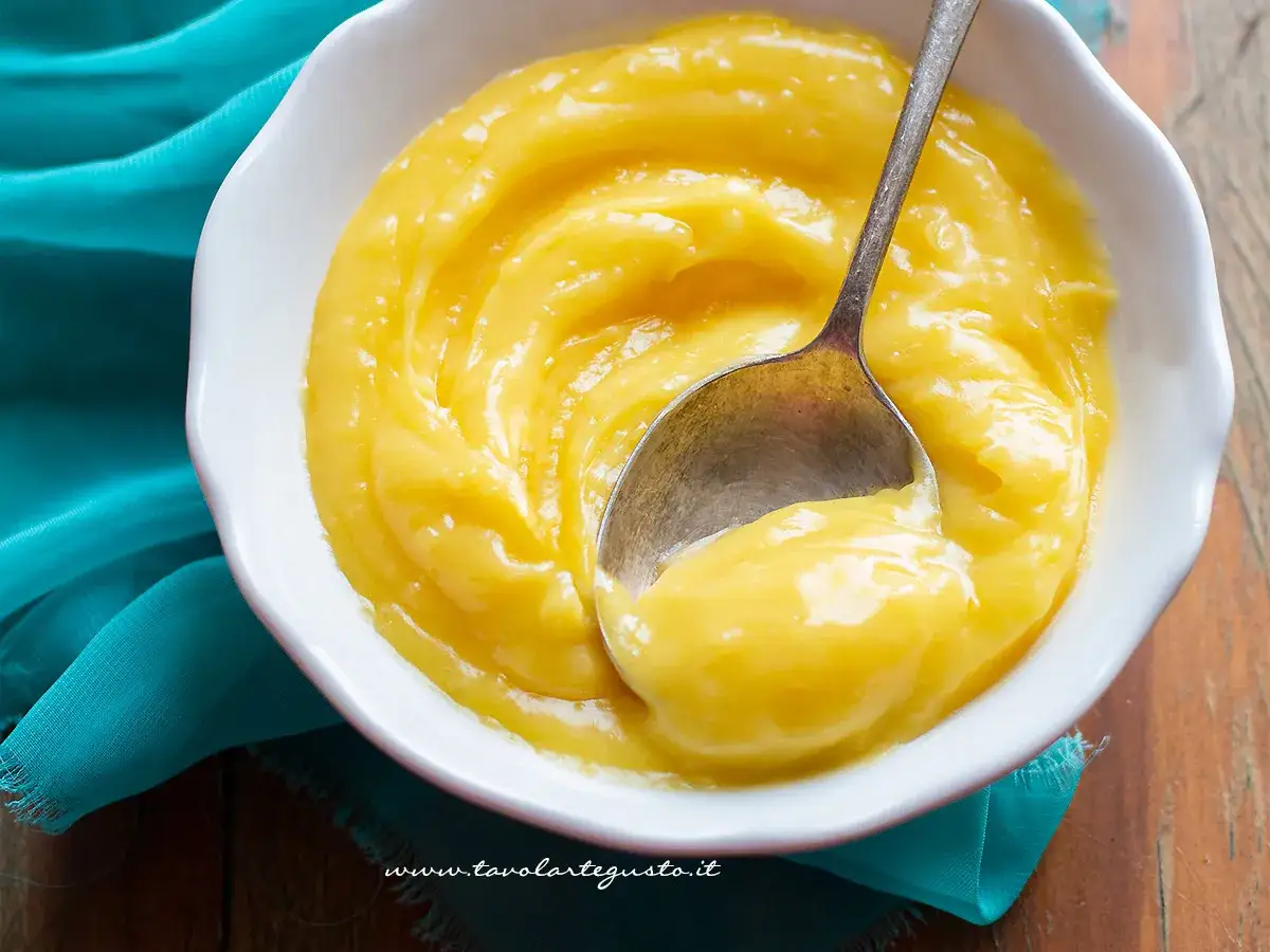 Una ciotola bianca piena di deliziosa crema al limone, con un cucchiaino che ne raccoglie una porzione.