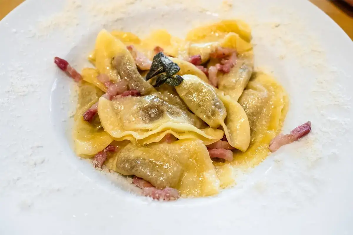 Piatto di casoncelli alla bergamasca con pancetta e salvia, spolverati di formaggio grattugiato.