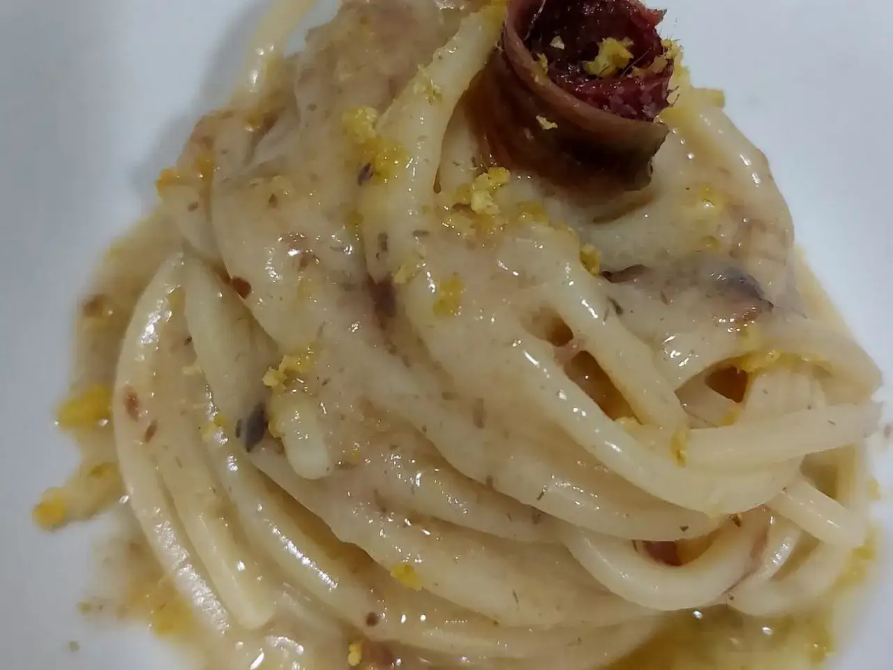 Spaghetti burro e alici, un piatto semplice ma gustoso, con un tocco di limone e un'alicia arrotolata in cima.