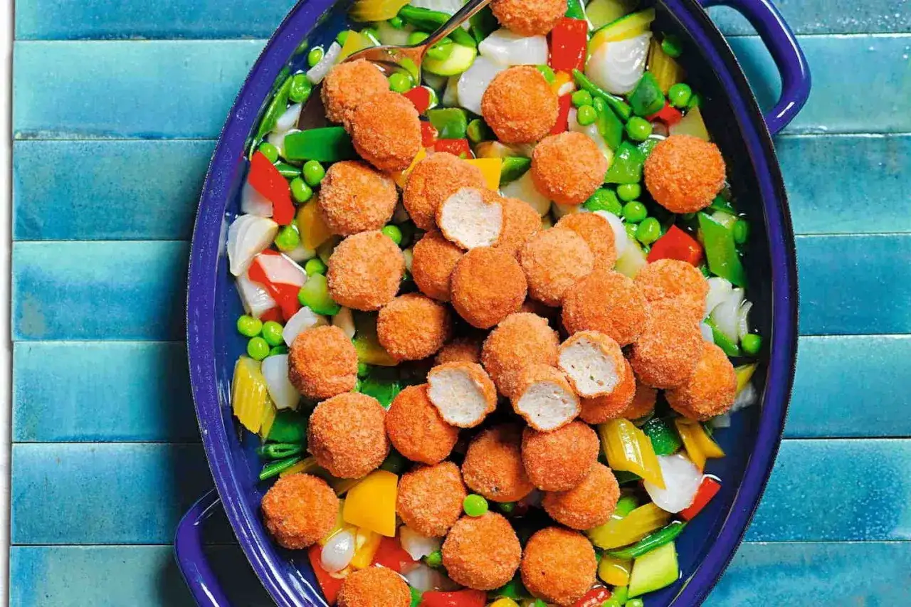 Crocchette di petto di pollo ricette: gustose palline dorate su un letto di verdure miste colorate in una ciotola blu.