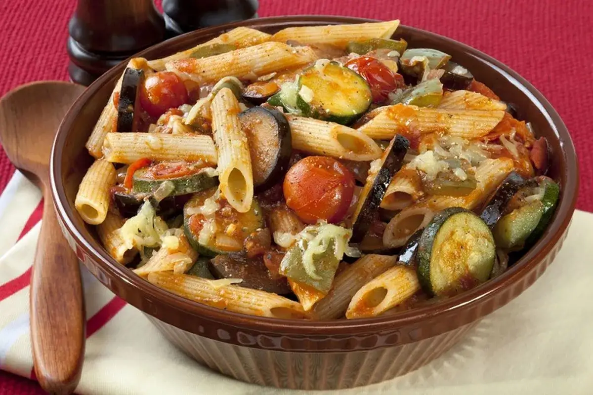Piatto invitante di pasta con verdure miste: melanzane, zucchine e pomodorini, condita con formaggio grattugiato.