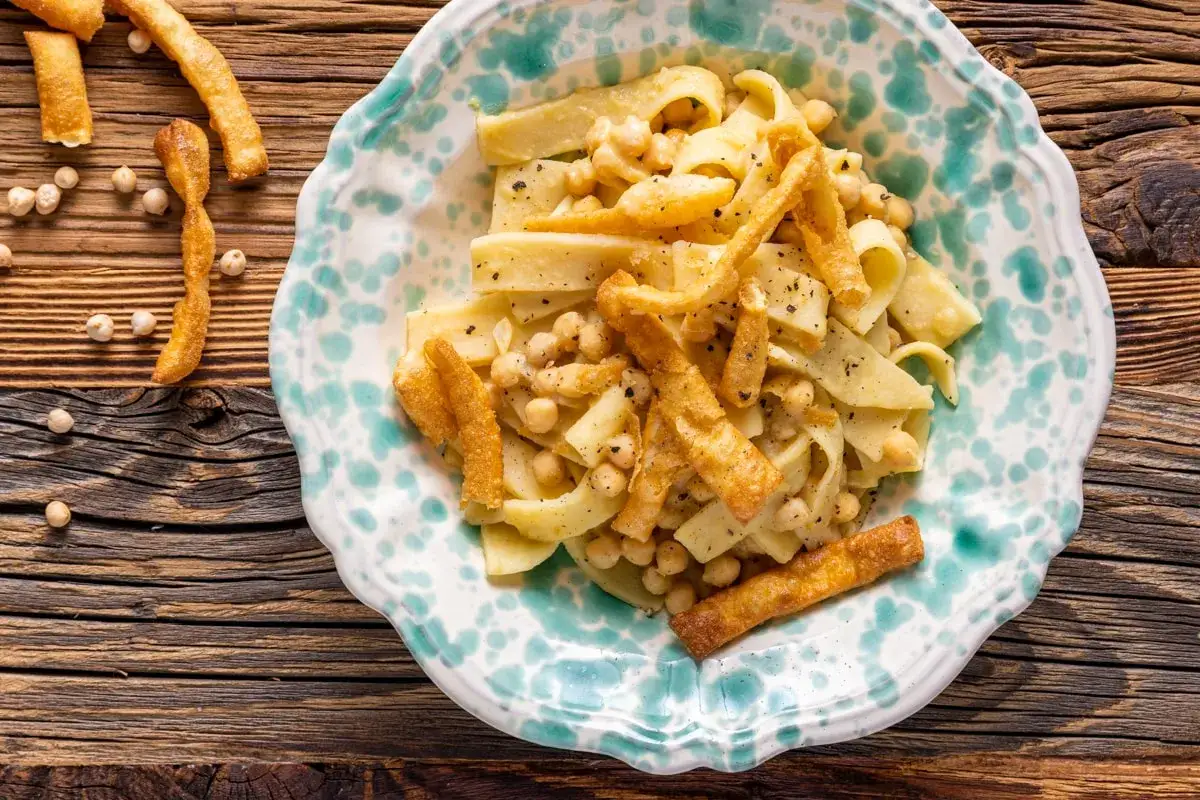Piatto di ciceri e tria, pasta fresca con ceci e croccanti strisce di pasta fritta, servito in un piatto decorato.