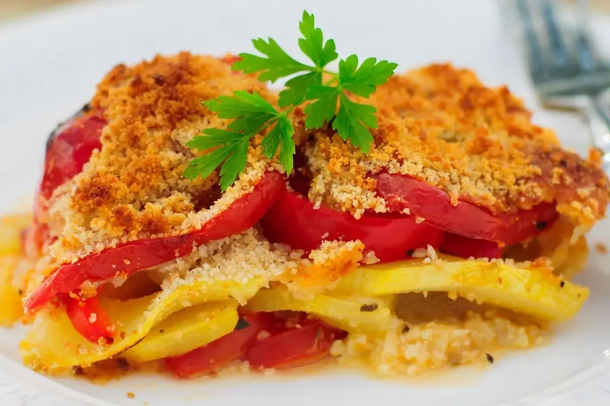 Peperoni gratinati in friggitrice ad aria, con strati di zucchine e pomodoro, guarniti con prezzemolo fresco e una croccante panatura.