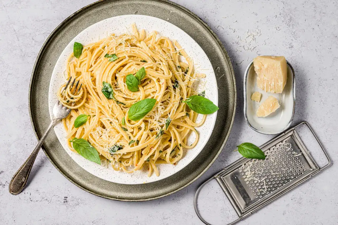 Un piatto di pasta al limone, guarnito con basilico fresco e parmigiano grattugiato, pronto per essere gustato.