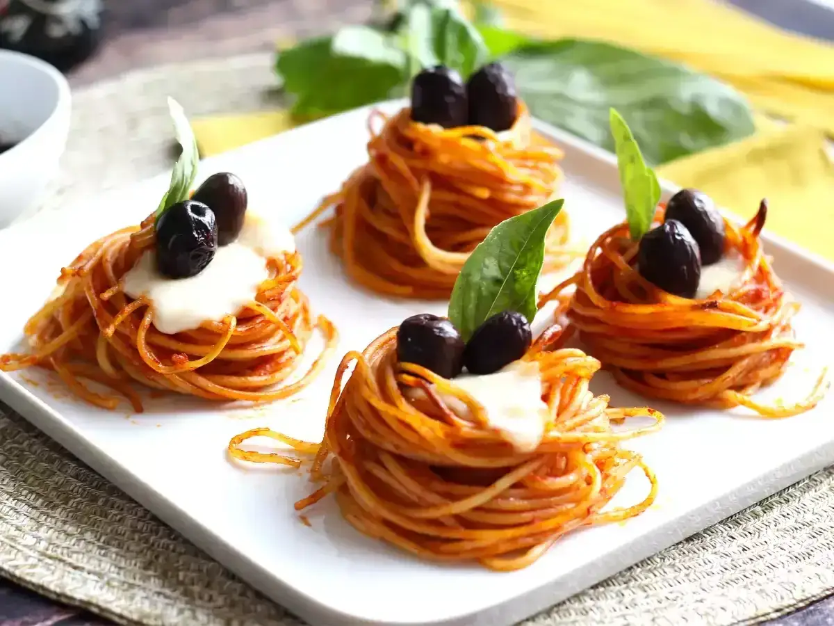 Nidi di spaghetti con sugo, mozzarella e olive nere, perfetti per ricette primi piatti sfiziosi.