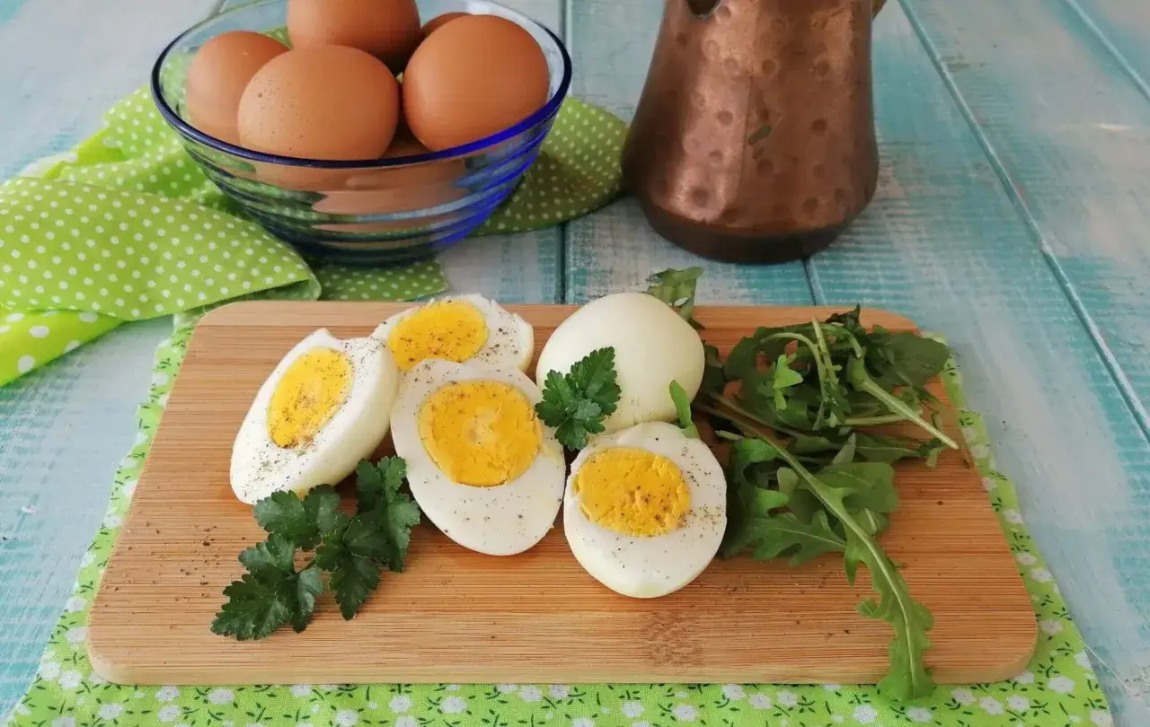 Uova sode in friggitrice ad aria, tagliate a met&agrave;, con un uovo intero, prezzemolo e rucola su un tagliere di legno.