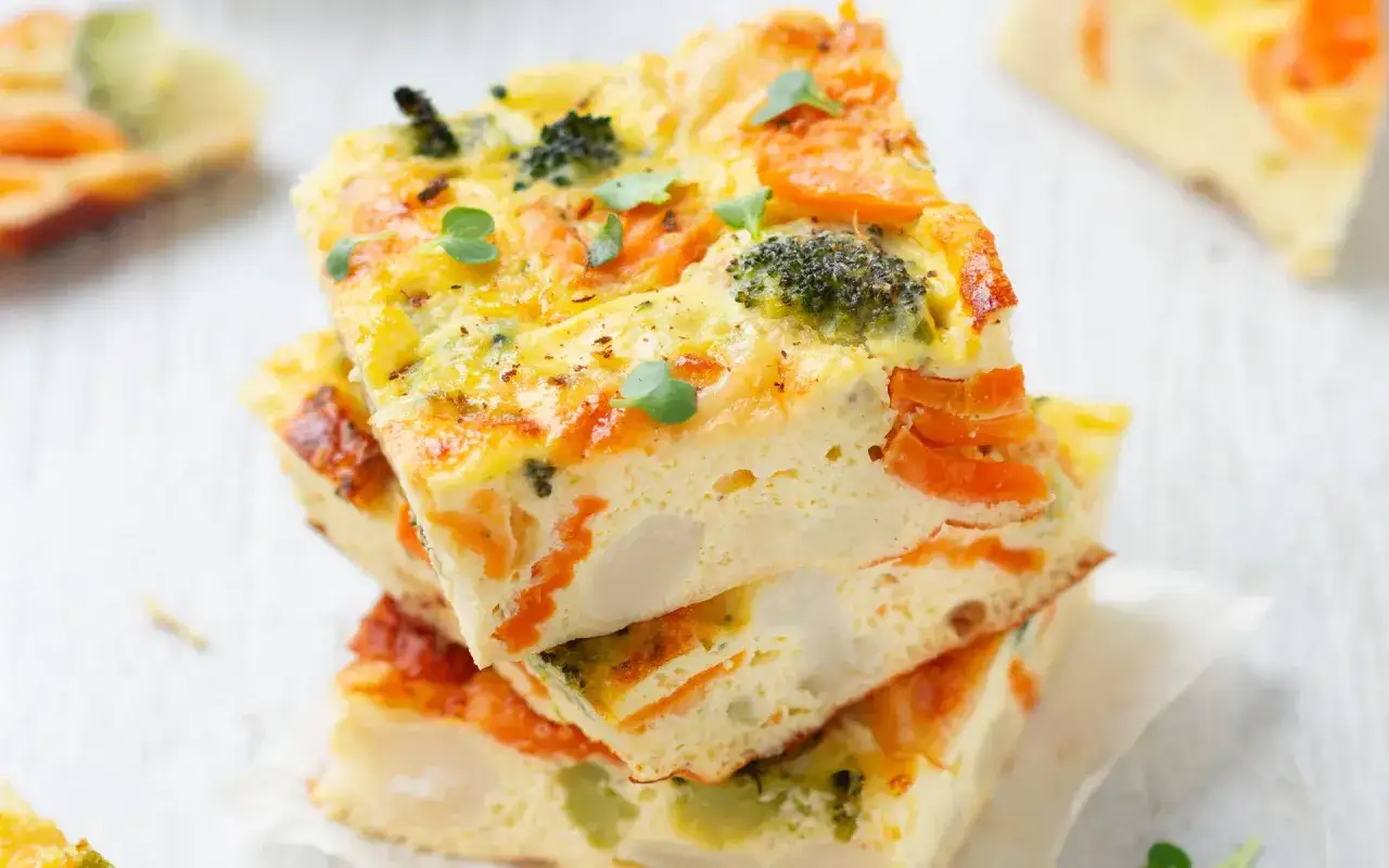 Fette di frittata al forno con broccoli e carote, guarnite con germogli freschi. Un piatto colorato e salutare.
