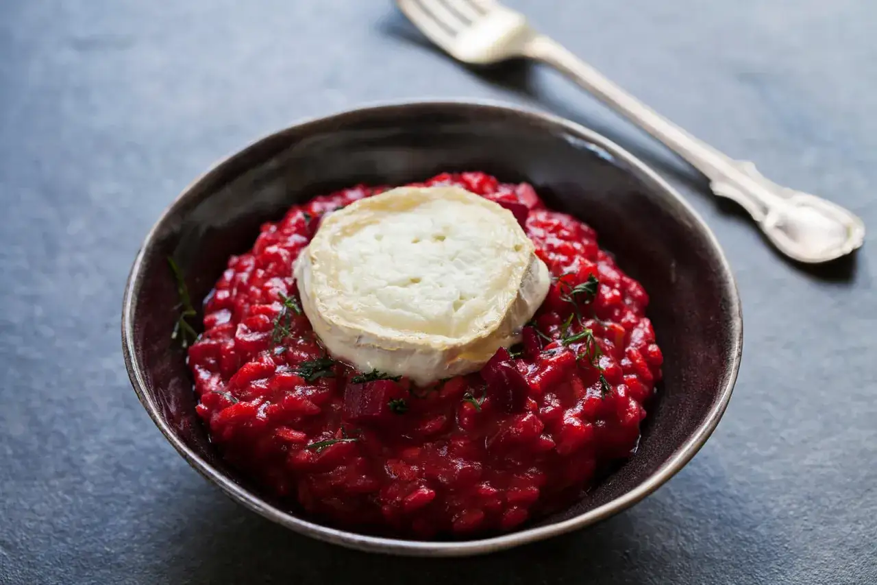 Risotto alla barbabietola cremoso, con una fetta di formaggio di capra fuso e erbe aromatiche.