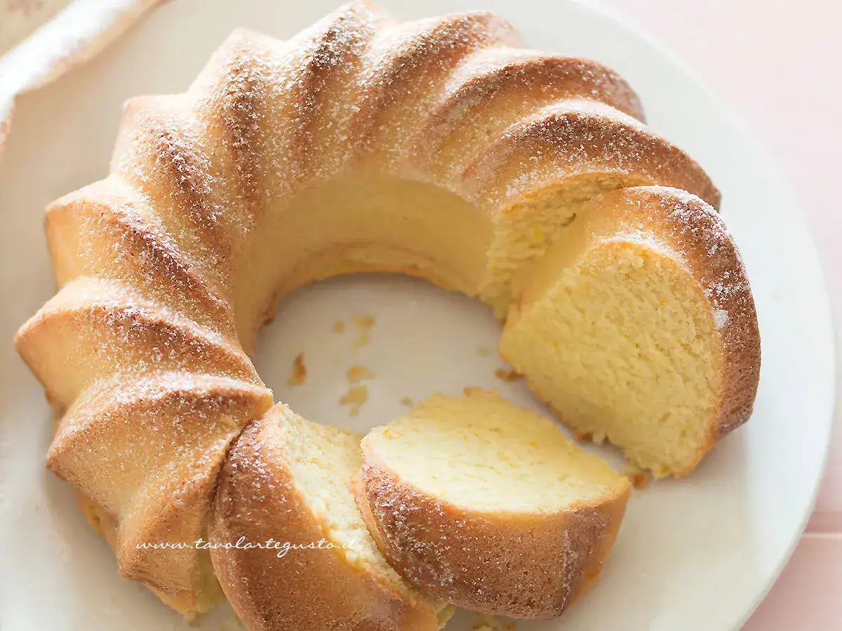 Una torta di ricotta sofficissima, a forma di ciambella, cosparsa di zucchero a velo. Le fette mostrano la sua incredibile morbidezza.
