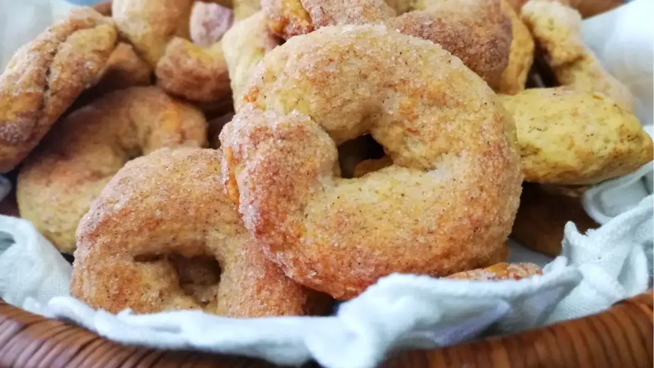 Ciambelline al vino friabilissime, dorate e cosparse di zucchero, riposano in un cestino foderato di bianco.