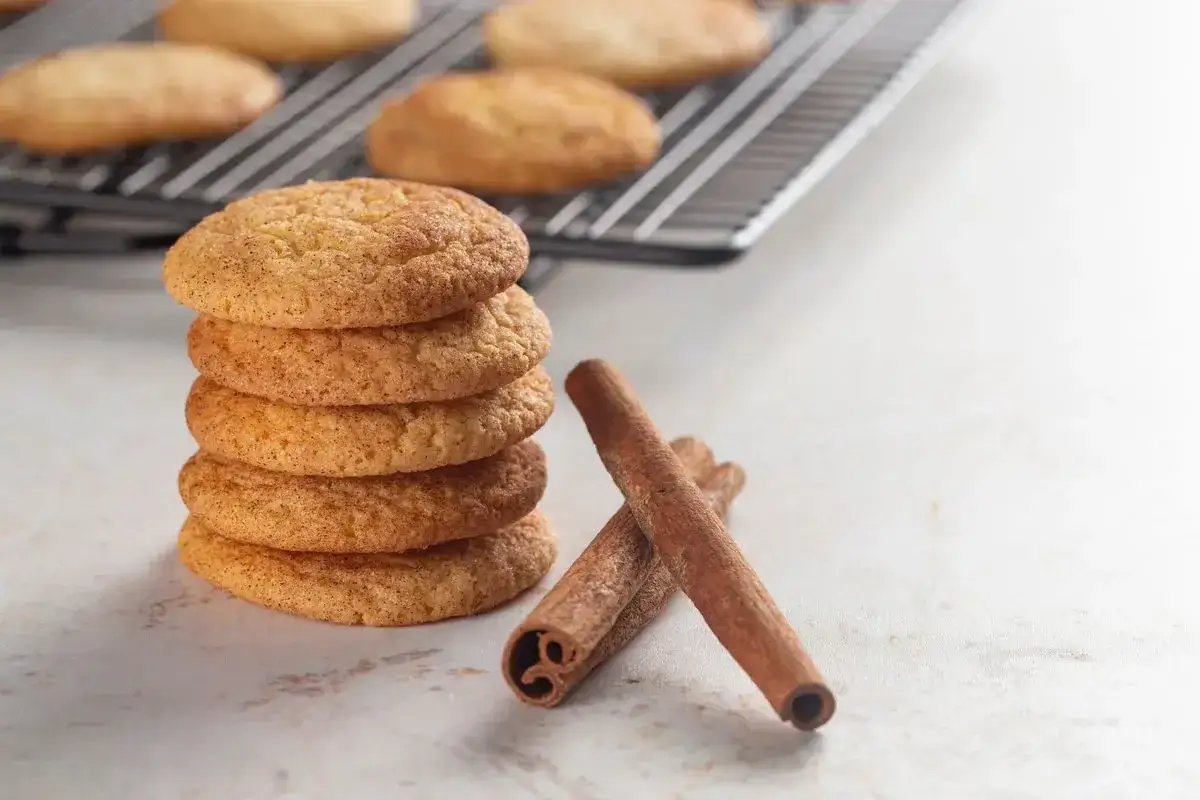 Una pila di biscotti alla cannella, cosparsi di zucchero e cannella, accanto a bastoncini di cannella su una superficie chiara.