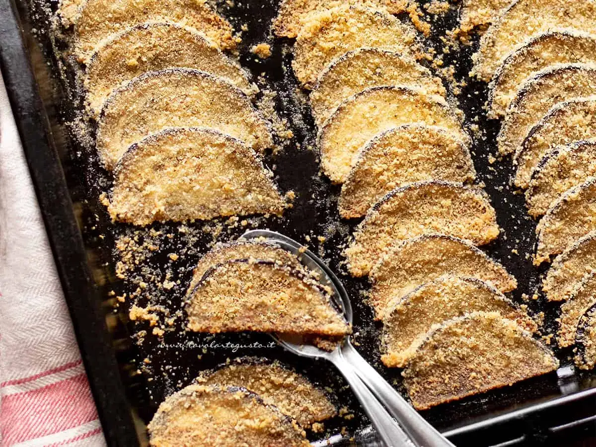 Fette di melanzane al forno, impanate e dorate, disposte su una teglia. Un piatto semplice e gustoso.