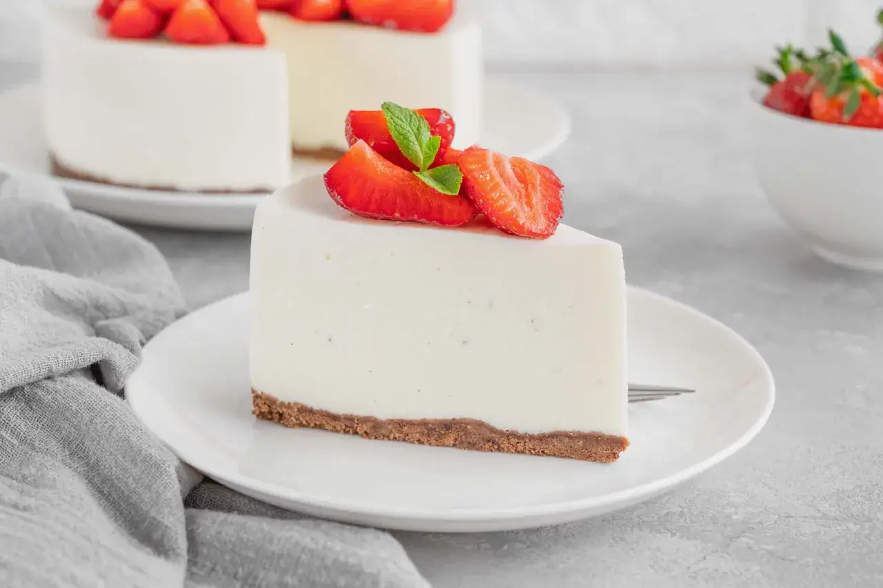 Una fetta di torta fredda allo yogurt, guarnita con fragole fresche e menta, su un piatto bianco.