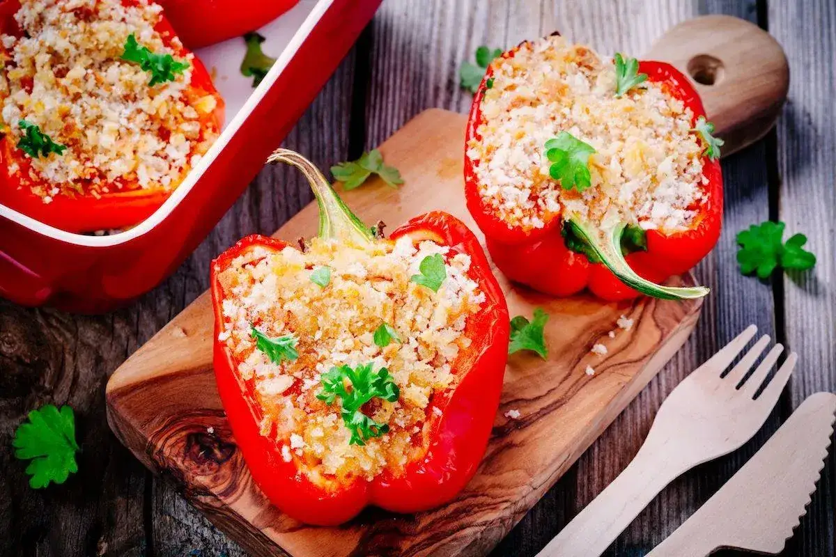 Peperoni ripieni senza carne, dorati e profumati, pronti per essere gustati su un tagliere di legno.