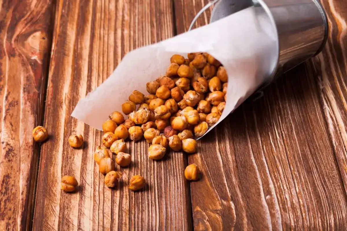 Ceci croccanti in friggitrice ad aria, versati da un sacchetto di carta su un tavolo di legno. Uno snack salutare e gustoso.