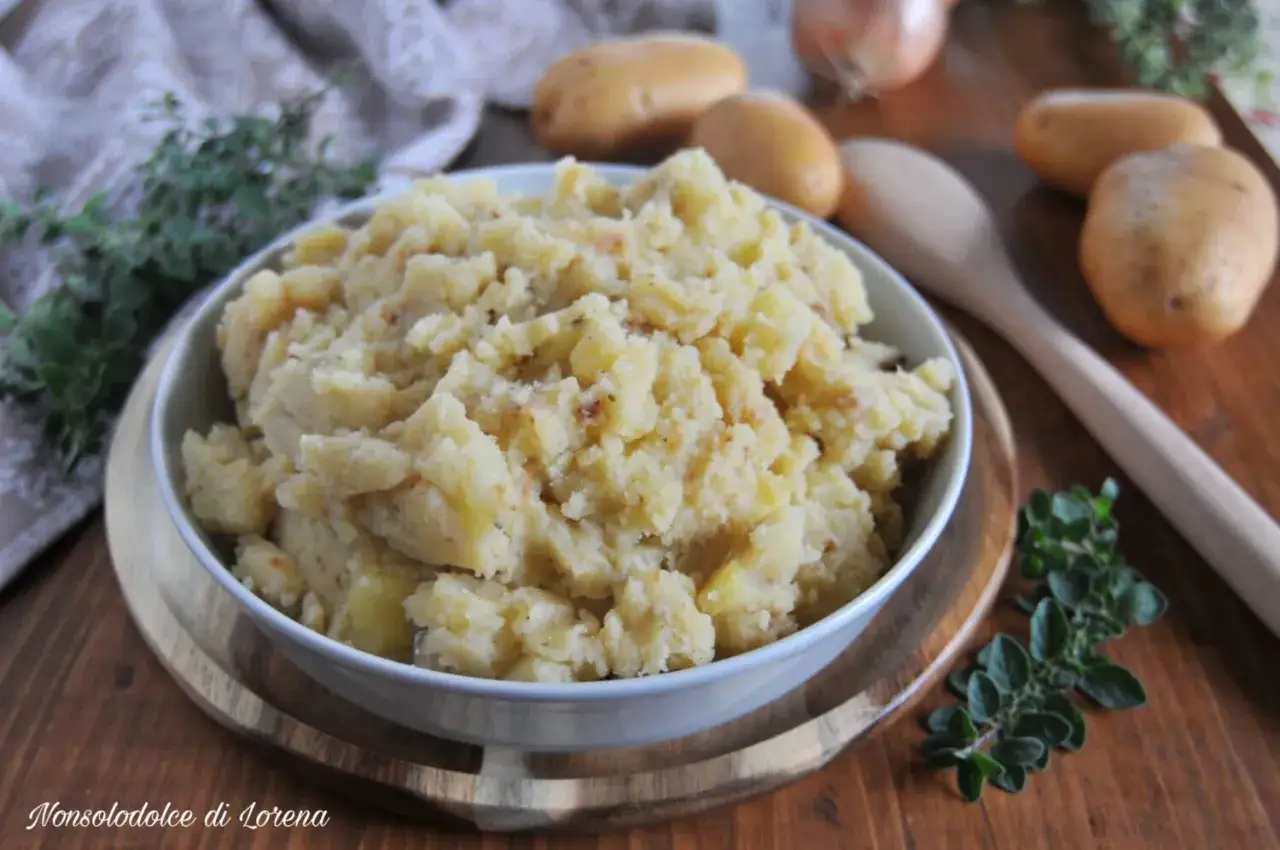 Un saporito piatto di patate in tecia, cotte con erbe aromatiche e spezie, servite in una ciotola su un tagliere di legno.