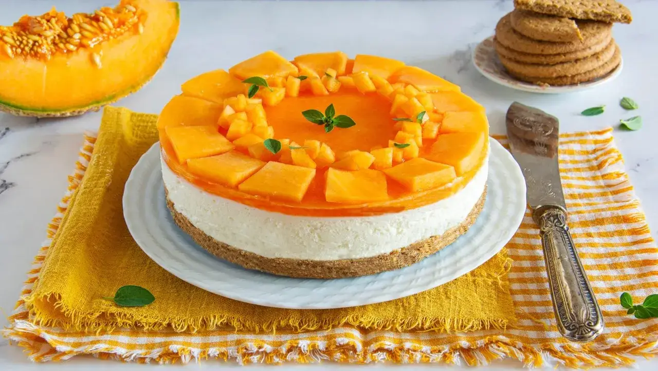 Deliziosa cheesecake al melone, con strato cremoso e topping di frutta fresca, guarnita con menta. Perfetta per l'estate.