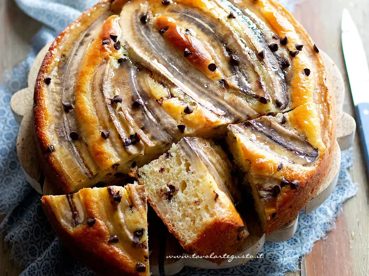 Delizioso dolce con banane caramellate e gocce di cioccolato, tagliato a fette su un tagliere di legno.
