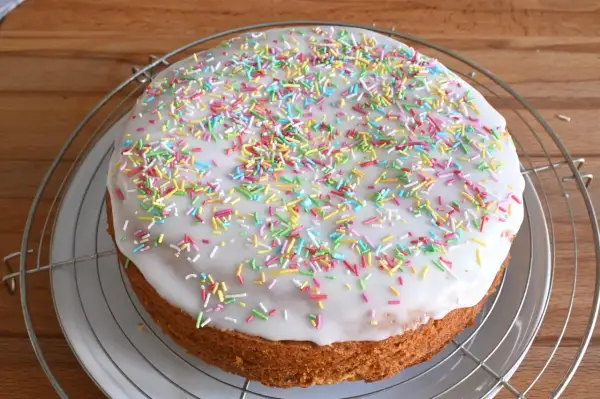Torta rotonda con glassa di zucchero bianca e confettini colorati, su una griglia metallica.