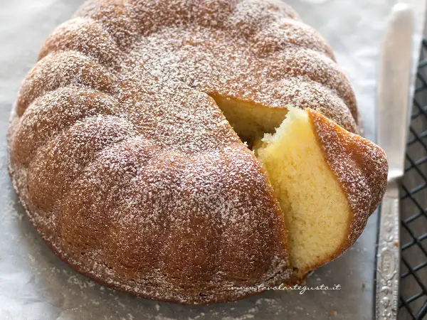 Una torta semplice e veloce, soffice e spolverata di zucchero a velo, con una fetta tagliata che ne mostra l'interno dorato.