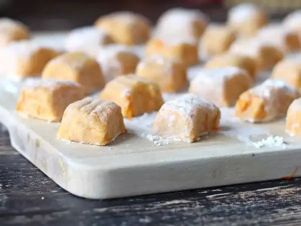 Gnocchi di zucca fatti in casa, morbidi e colorati, pronti per essere cucinati su un tagliere di legno.
