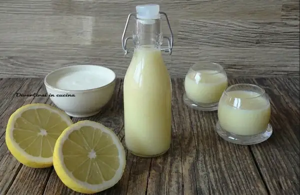 Una bottiglia e due bicchierini di crema di limoncello, con limoni freschi e una ciotola di panna.