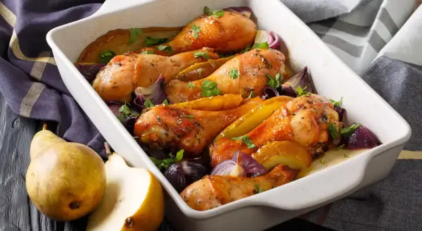 Cosce di pollo al forno croccante con pere e cipolle rosse in una teglia bianca.