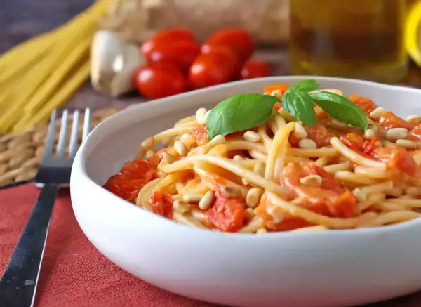Un piatto invitante di spaghetti con pomodorini freschi, pinoli tostati e basilico, pronto per essere gustato.