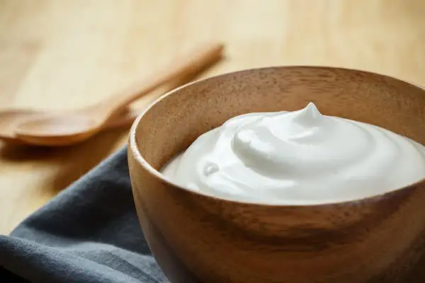 Una ciotola di legno piena di soffice crema al latte, pronta per essere gustata. Due cucchiai di legno sullo sfondo.