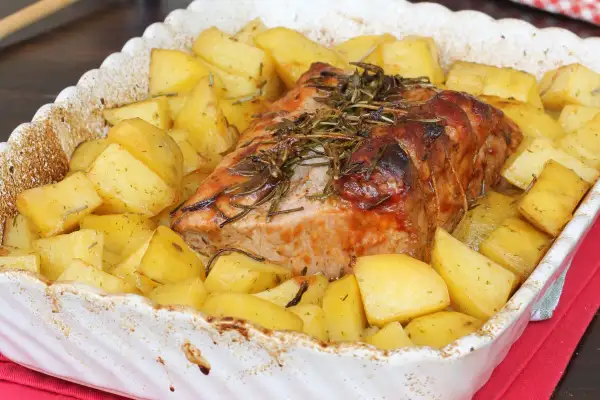Arrosto di maiale succulento cotto al forno con patate dorate e rosmarino, un piatto invitante pronto per essere gustato.