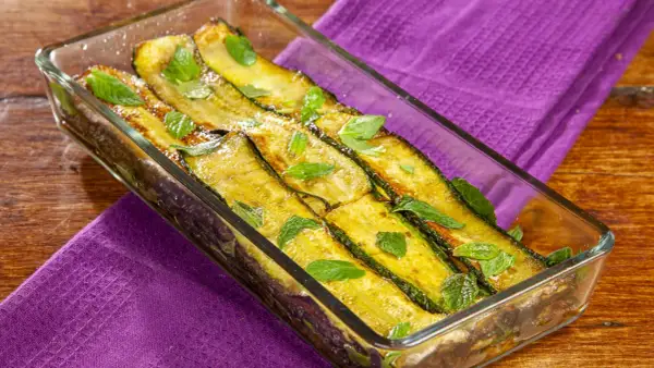 Zucchine alla scapece dorate e profumate, guarnite con foglie di menta fresca in una pirofila di vetro su un tavolo di legno.