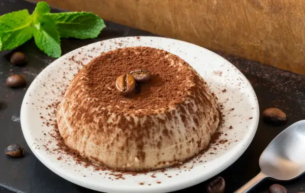 Deliziosa panna cotta al caffè, cosparsa di cacao e decorata con chicchi di caffè e menta fresca.