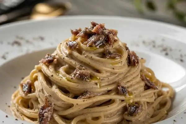 Spaghetti burro e alici, un piatto cremoso e saporito, con fili di pasta avvolti in una salsa delicata e guarniti con pezzetti di acciughe.