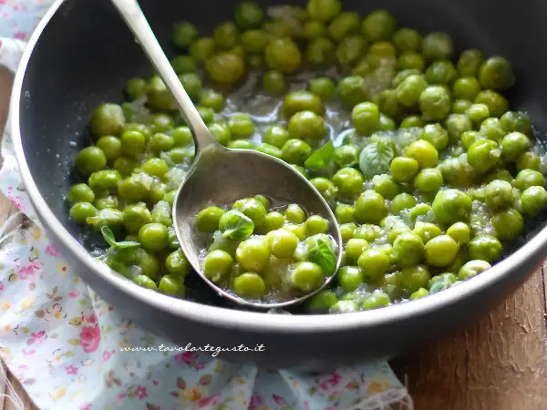 Piselli freschi in padella, cotti con cipolla e menta. Un cucchiaio ne raccoglie una porzione invitante.