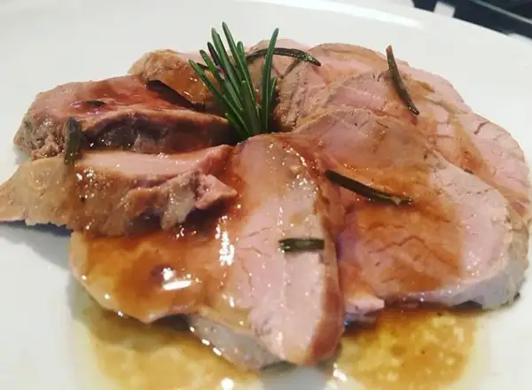 Fette succulente di filetto di maiale al forno, bagnate in un sughetto saporito e guarnite con rosmarino fresco.