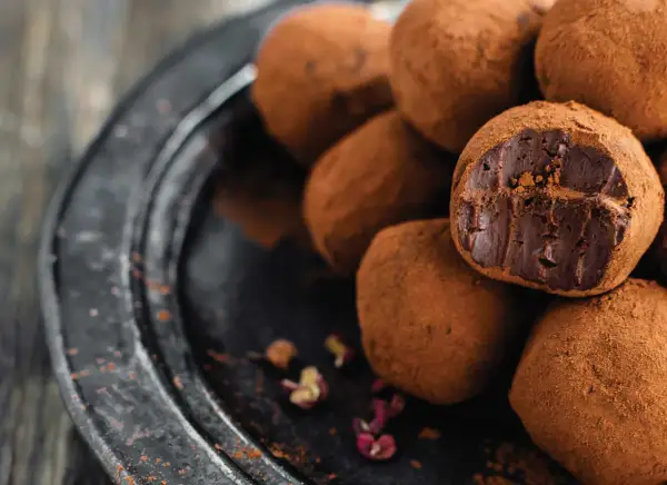Un mucchio di tartufini al cioccolato ricoperti di cacao, uno aperto rivela il ripieno fondente.
