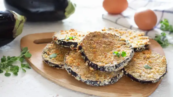 Fette di melanzane al forno impanate, dorate e croccanti, guarnite con erbe aromatiche fresche.