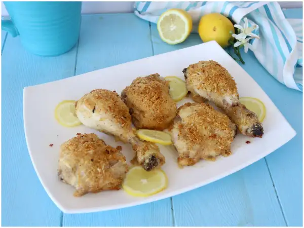 Cosce di pollo al limone croccanti e dorate, servite su un piatto bianco con fette di limone fresco.