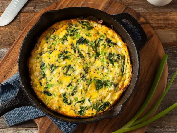 Frittata al forno con spinaci e cipollotti, appena sfornata in padella di ghisa, pronta per essere gustata.