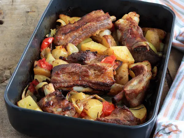 Puntine di maiale succulente al forno con patate, peperoni e cipolle in una teglia scura.
