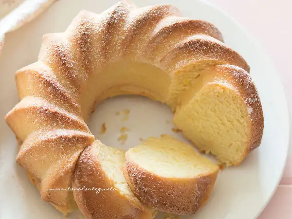 Una torta di ricotta sofficissima, dorata e cosparsa di zucchero a velo, tagliata a fette su un piatto bianco.