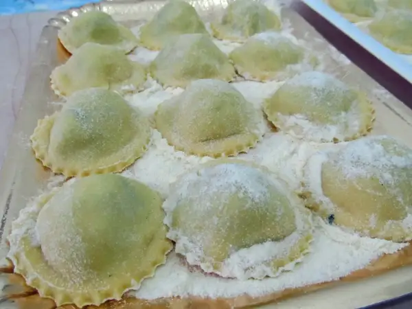 Un vassoio pieno di ravioli ricotta e spinaci freschi, spolverati di farina, pronti per essere cucinati.