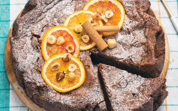 Torta di pane al cioccolato, decorata con fette d'arancia, nocciole e cannella, spolverata di zucchero a velo.