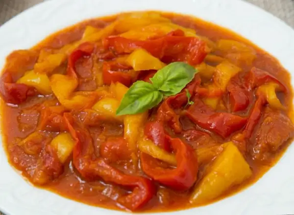 Peperonata ricetta della nonna: peperoni rossi e gialli cotti lentamente in un sugo saporito, guarniti con una foglia di basilico fresco.