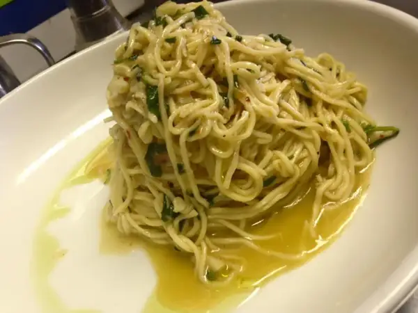 Un piatto di spaghetti aglio olio e peperoncino cremosi, conditi con prezzemolo fresco e un filo d'olio d'oliva, serviti in una ciotola bianca.