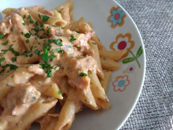 Penne al baffo cremose e saporite, condite con una salsa rosa e prezzemolo fresco, servite su un piatto decorato con fiori.