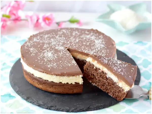 Deliziosa torta cocco e cioccolato, con una fetta appena tagliata, cosparsa di cocco grattugiato.