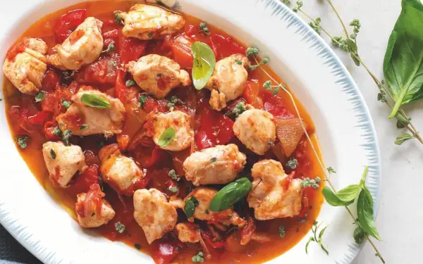Piatto di coniglio alla cacciatora ricetta della nonna, con pezzi di carne tenera in salsa di pomodoro e peperoni, guarnito con basilico fresco e timo.