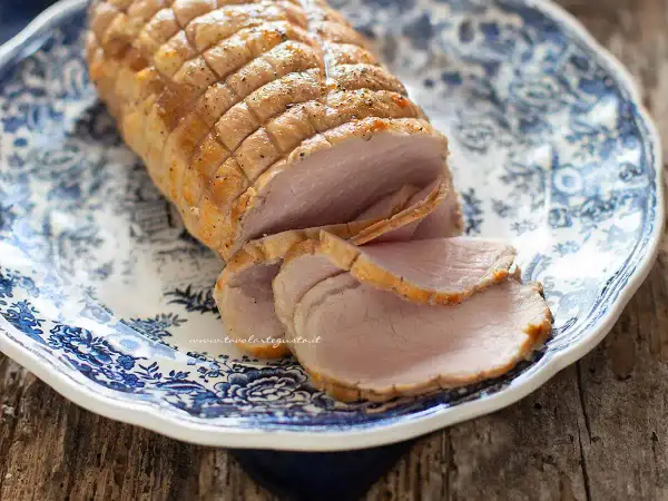 Arrosto di maiale morbido con sughetto, affettato su un piatto decorato con motivi blu. Perfetto per un pranzo domenicale.