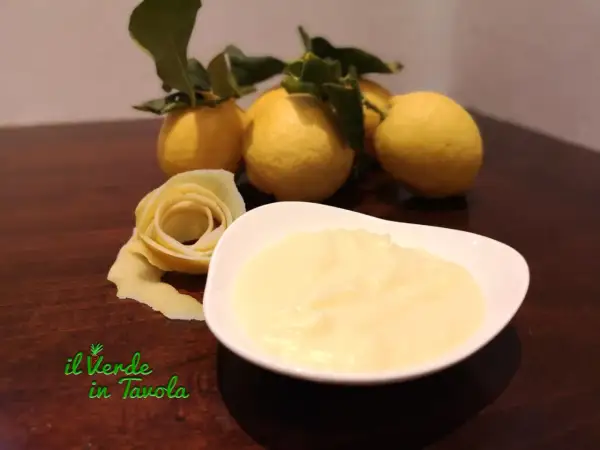 Una ciotola di cremosa crema al limone, con limoni freschi e una decorazione a forma di rosa fatta con la scorza.